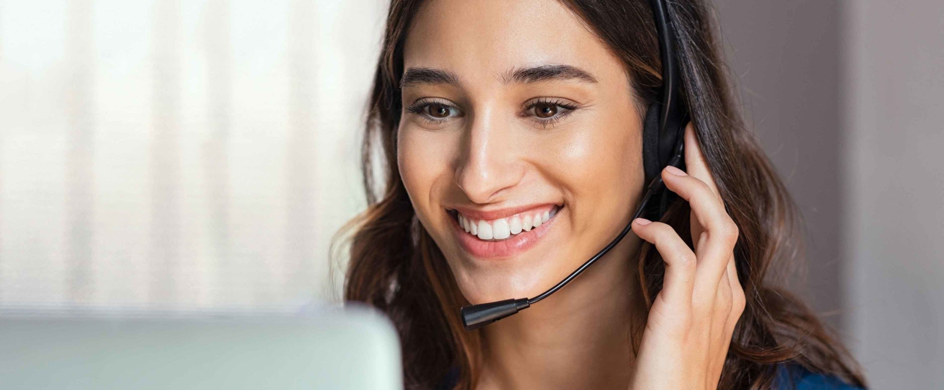 A woman wearing a headset and smiling at a computer