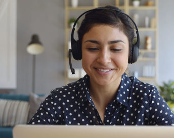 a woman wearing a headset and smiling at a computer screen