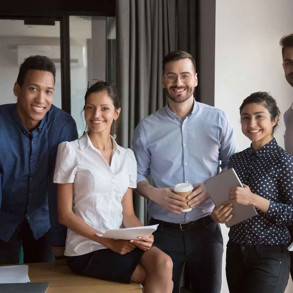 Five employees posing for a group photo in the workplace